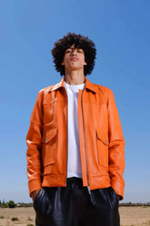 a young boy with curly hair wearing a Designer men’s orange leather trucker jacket with flap chest pockets, and welt side pockets.