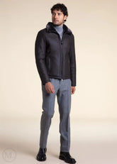 Man wearing a dark grey leather aviator jacket and gray pants on a beige background