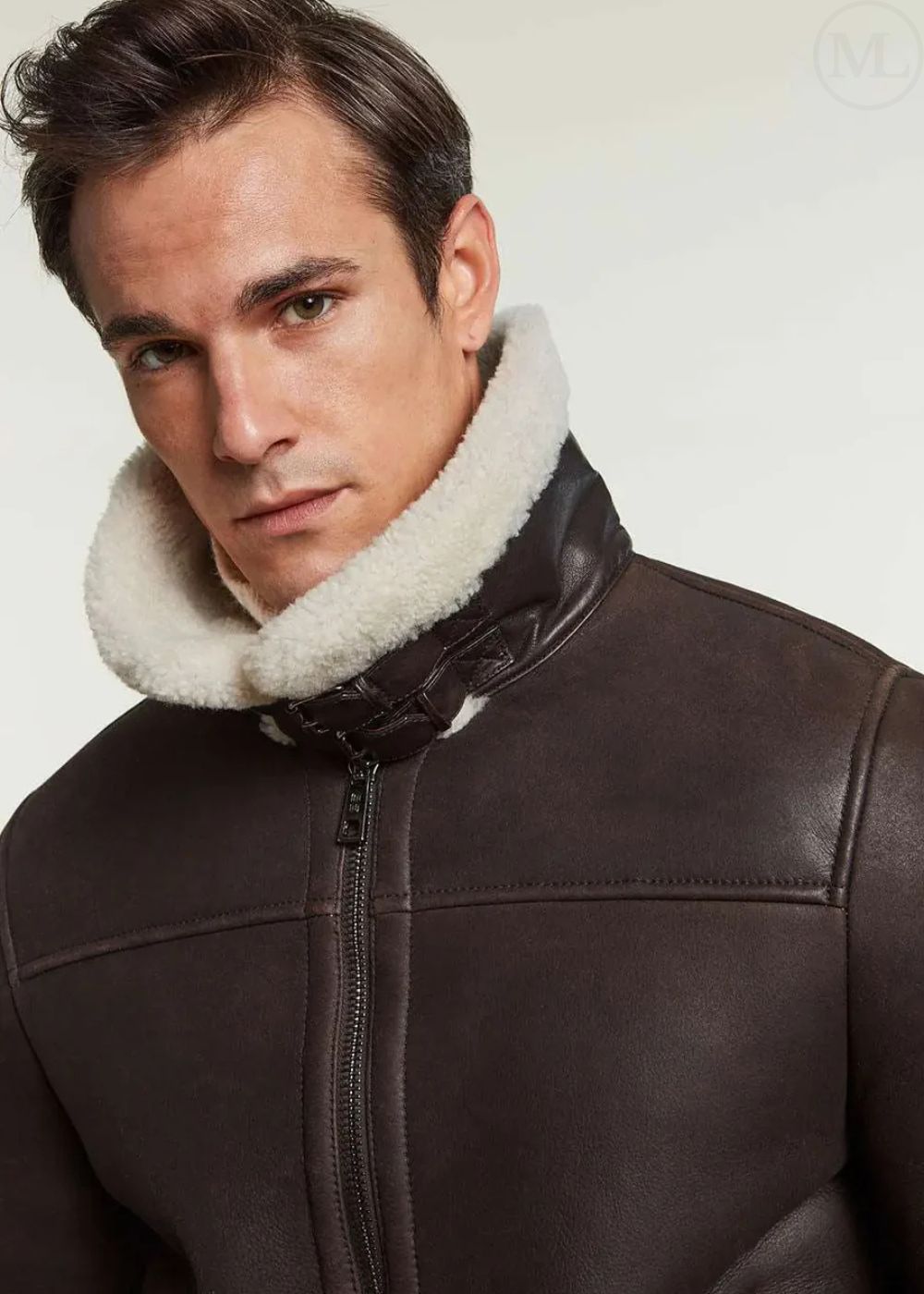 Man wearing a brown aviator leather jacket with a white fur collar against a plain background