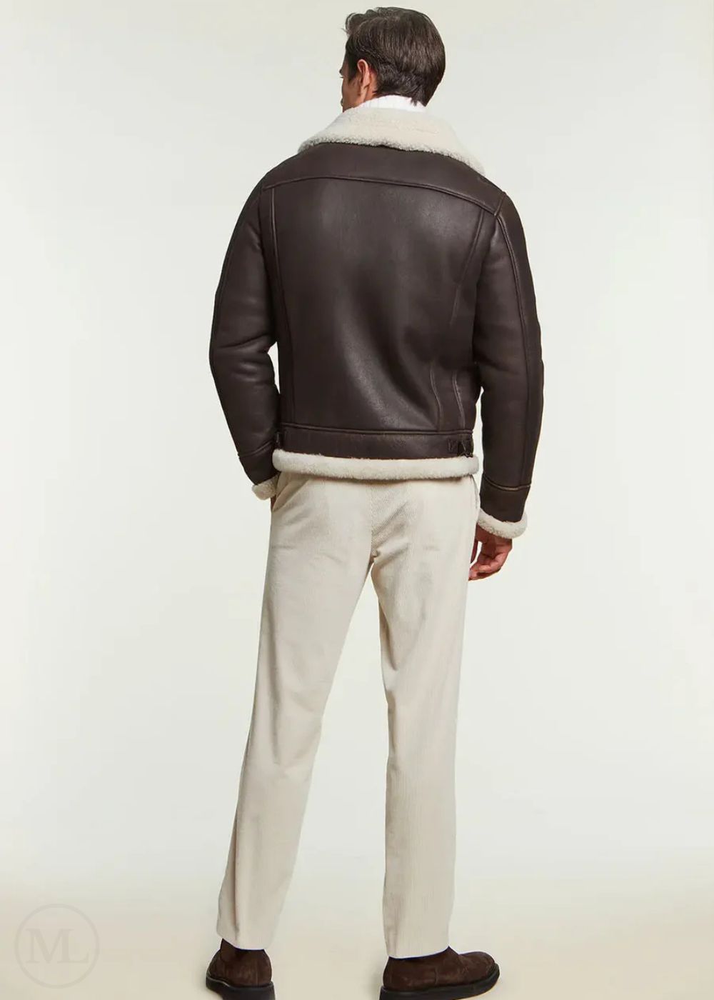 Man wearing a brown leather aviator jacket with white fur collar and cream pants on a white background