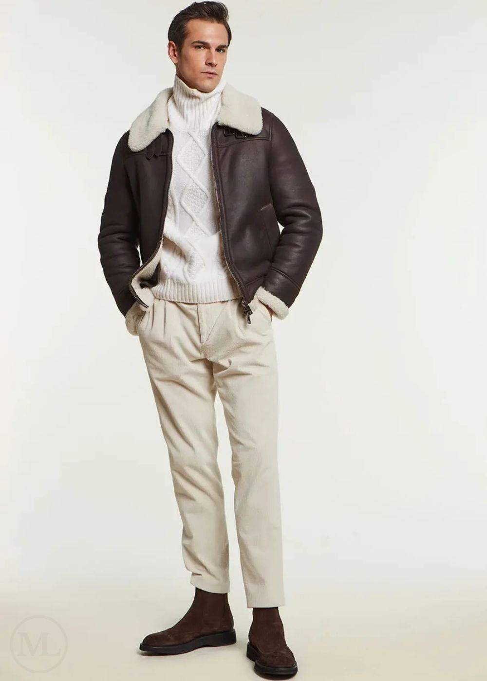 Man wearing a brown aviator leather jacket with fur collar, white turtleneck sweater, beige pants, and brown shoes on a white background.
