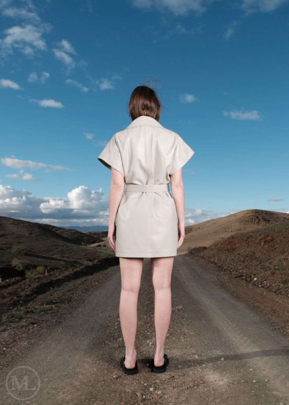 Women, ivory leather dress standing on a road with a scenic landscape and blue sky. back shot